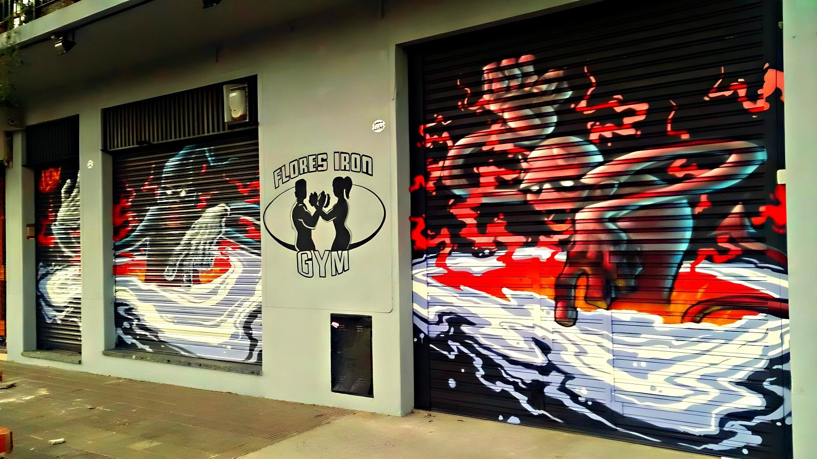 El frente del gimnasio sobre Av. Directorio, con el mural de Flores Iron Gym pintado en las cortinas